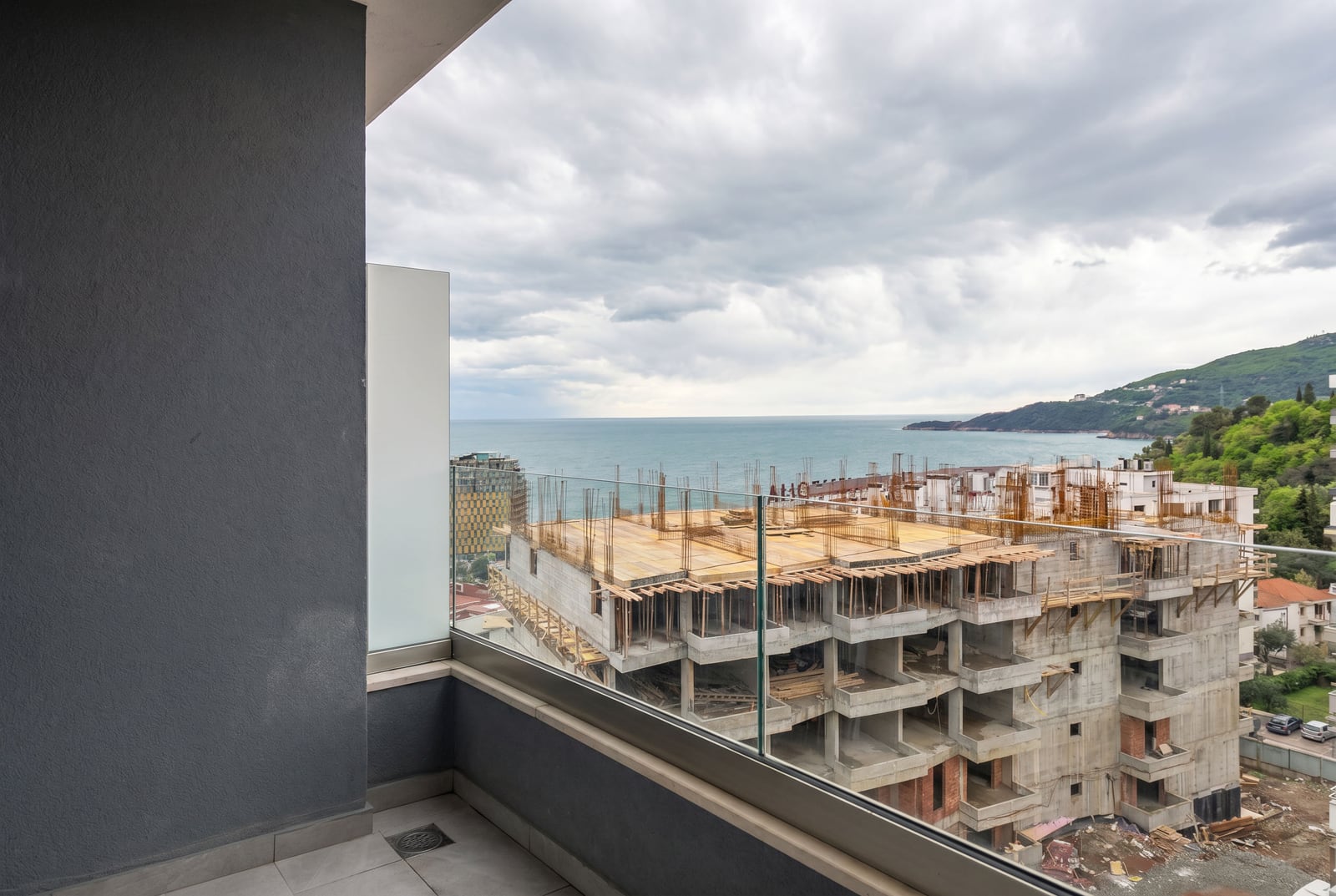 View from the balcony of a modern apartment in Bečići, Montenegro: panoramic sea view and a residential complex under construction nearby.