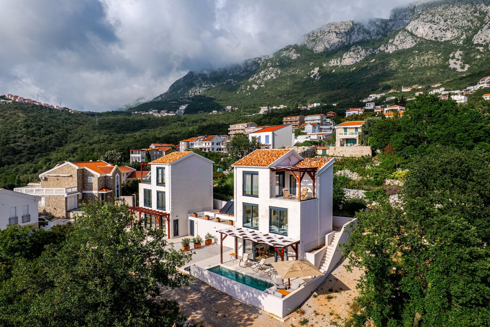 Savremene vile sa bazenom i krovom od crepa u pozadini planina u Blizikuči, Crna Gora