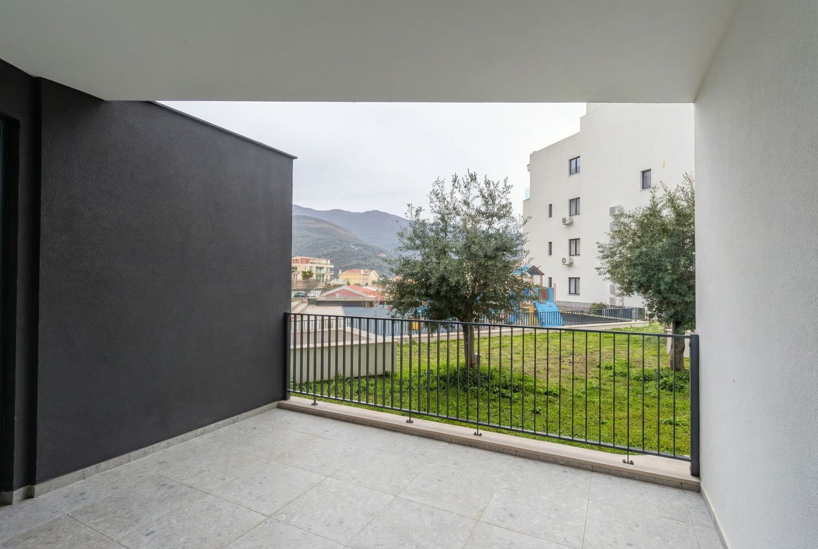 Prostran balkon s pogledom na planine i zeleni dvorište u modernom stanu, grad Bečići, Crna Gora.