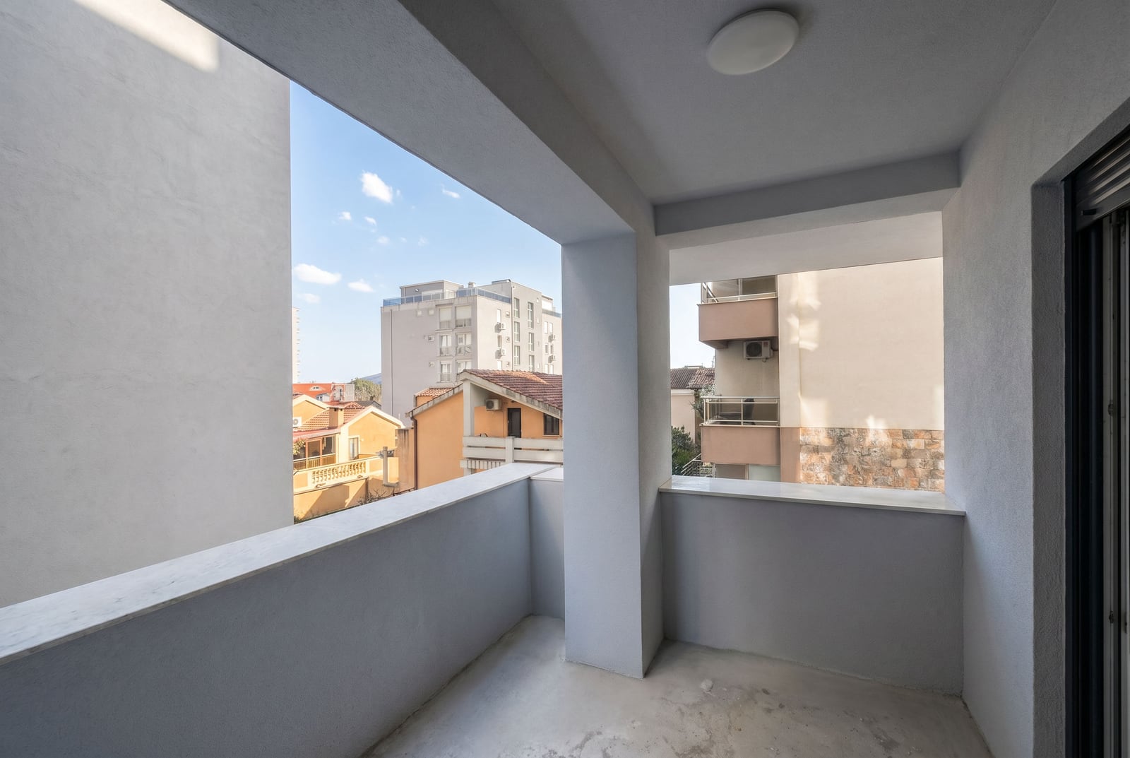 Prostran balkon sa modernom završnom obradom u stanu u Budvi, Crna Gora, sa pogledom na gradsko naselje.