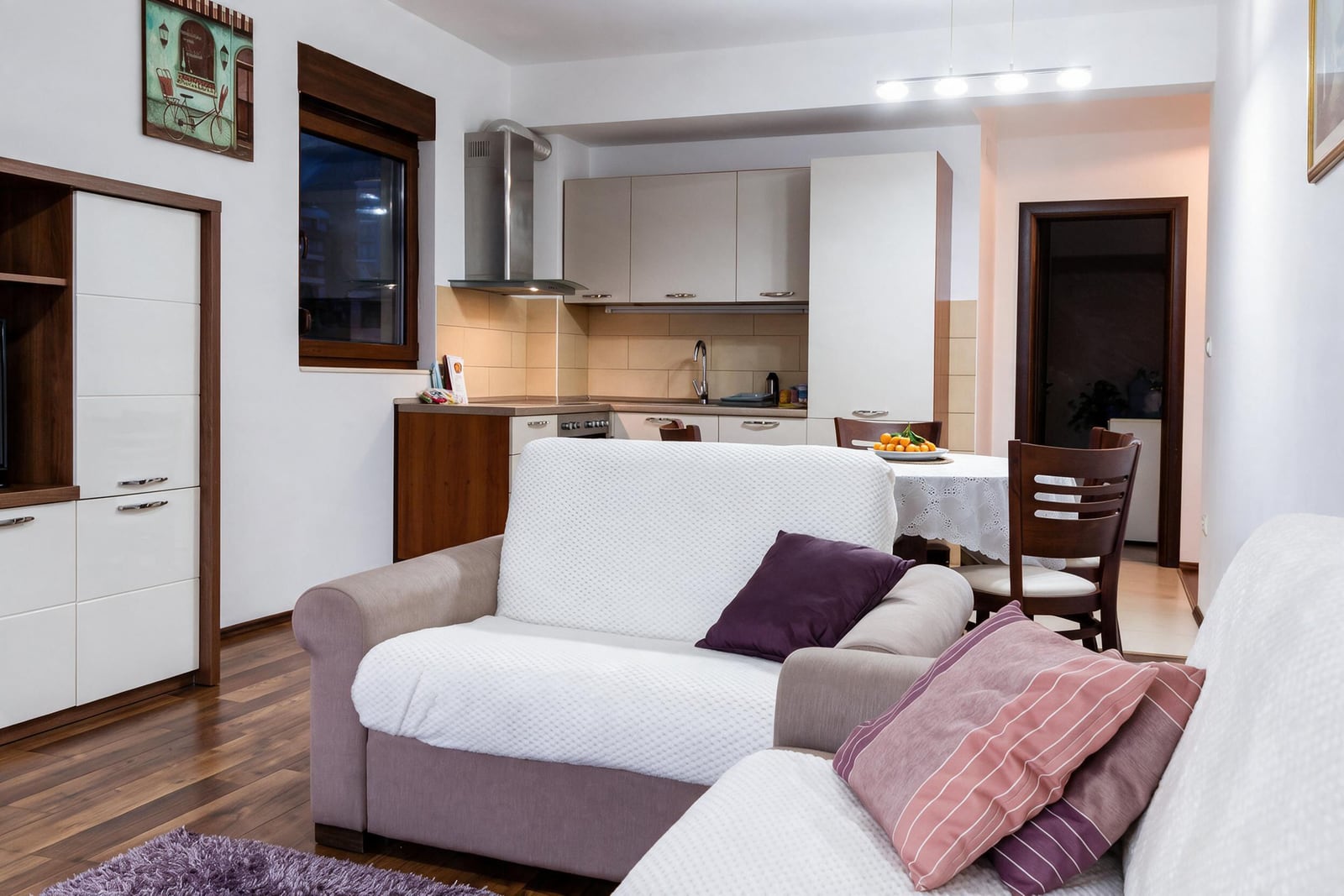 Modern living room with white sofas, kitchen, and dining area in an apartment in Budva, Montenegro
