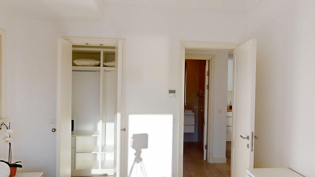 Helles Schlafzimmer in einer Wohnung, Luštica, Montenegro: Einbauschrank mit Regalen, weiße Türen und Durchgang zum Badezimmer.