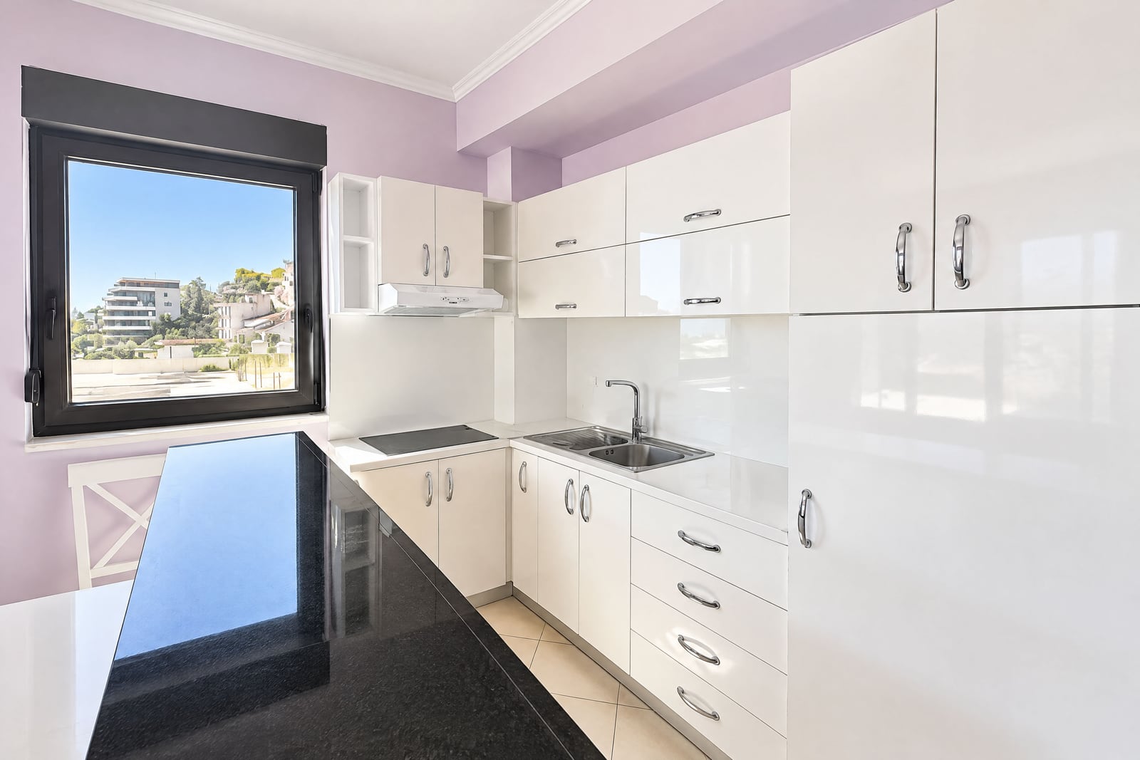 Modern white kitchen with glossy cabinets, black countertop, and a window view in an apartment in Budva, Montenegro