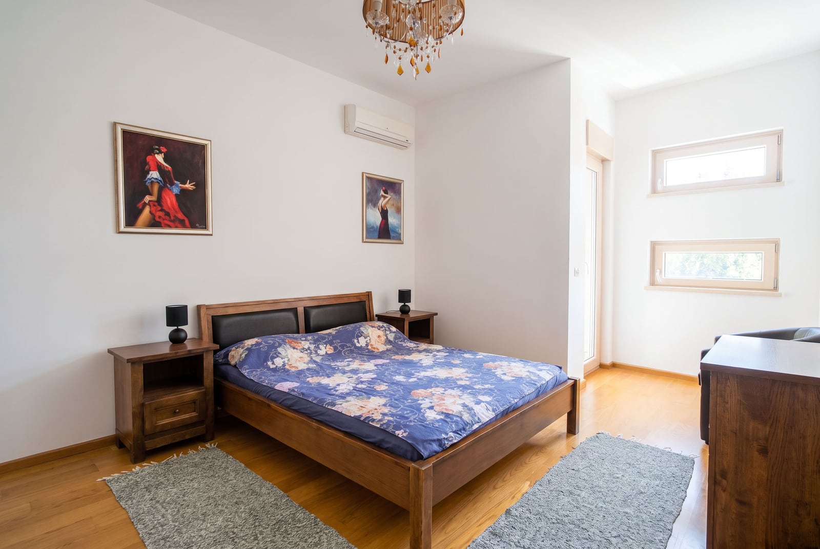 Bedroom with a wooden bed, nightstands, and paintings in an apartment in Bečići, Montenegro.