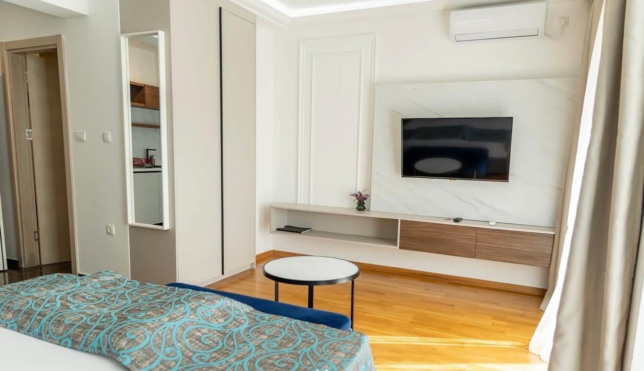 Modern bedroom in an apartment in Becici, Montenegro: light-toned finishes, TV area with a marble panel, and parquet flooring.