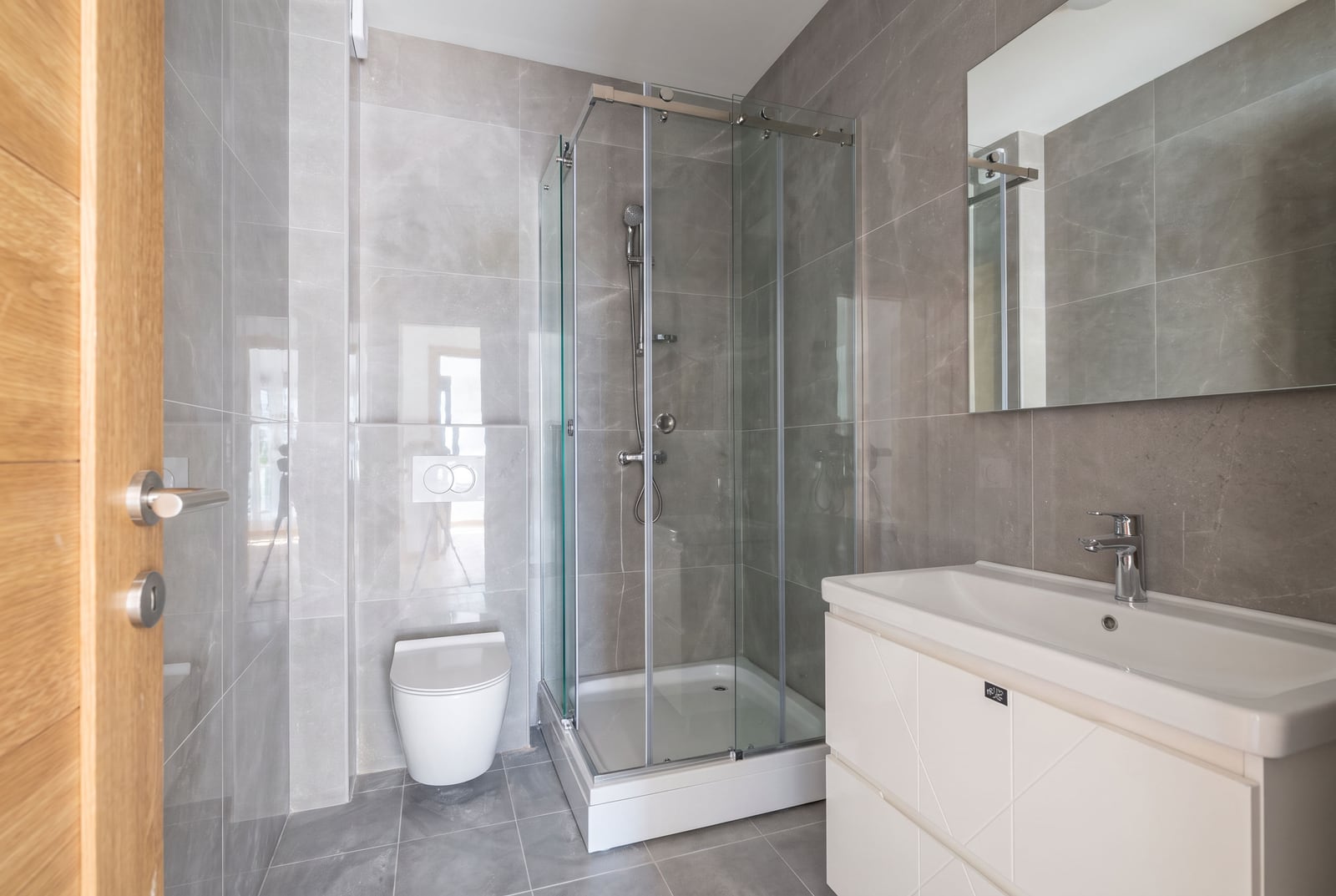 Modern bathroom in an apartment in the city of Bar, Montenegro: shower cabin, wall-hung toilet, and a vanity unit with a sink.