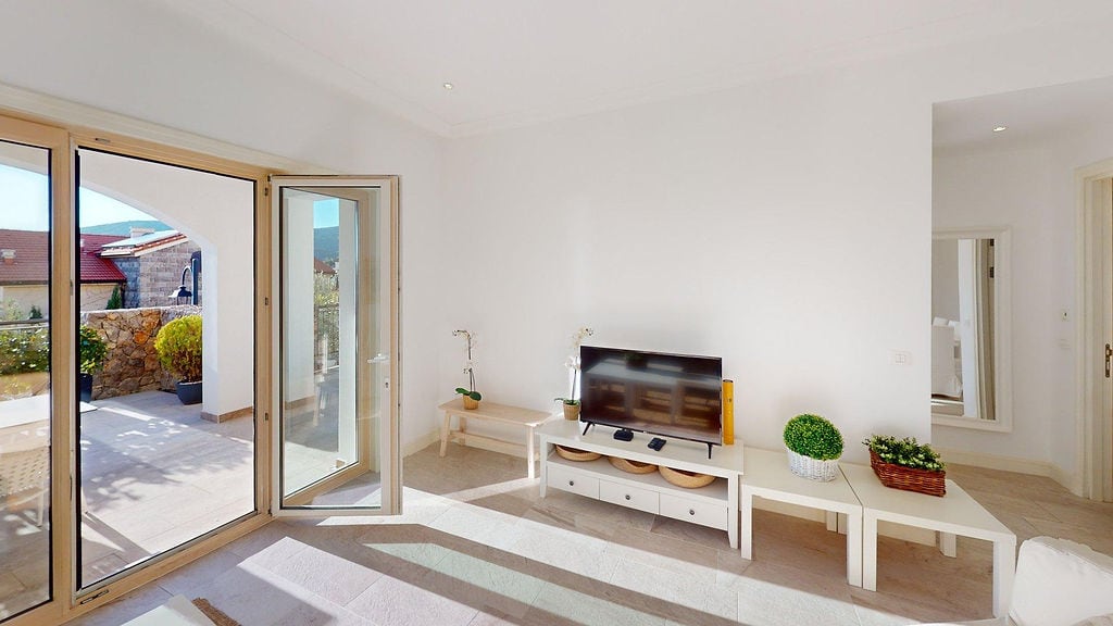 Helles Wohnzimmer mit Zugang zur Terrasse im Wohnkomplex, Luštica, Montenegro: weiße Möbel, TV-Bereich und Panoramafenster.