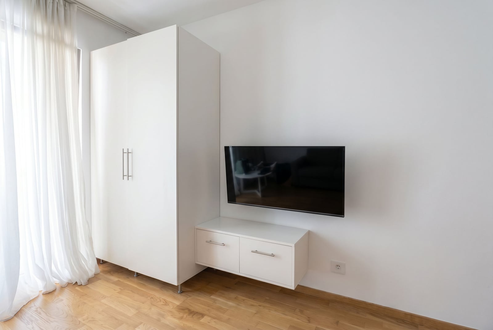 Modernes Wohnzimmer mit weißem Schrank, Sideboard und TV in einer Wohnung in Bečići, Montenegro. Heller Innenraum mit Parkettboden.