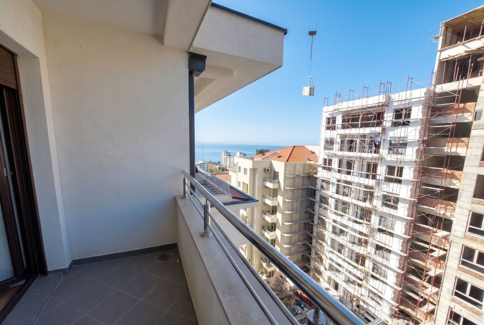Balkon apartamentu w Rafailovici, Czarnogóra, z widokiem na morze oraz powstające budynki mieszkalne z metalowym rusztowaniem.