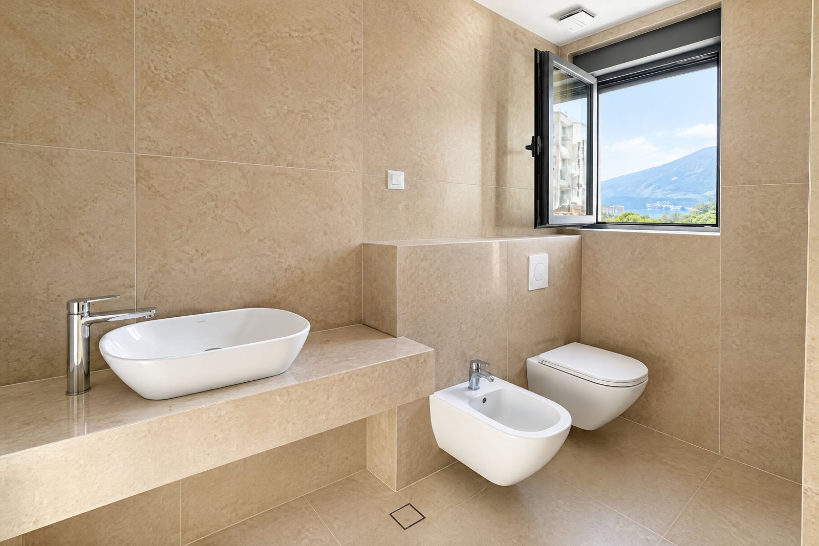 Modern bathroom with white fixtures, beige tiles, and mountain views in an apartment in Becici, Montenegro