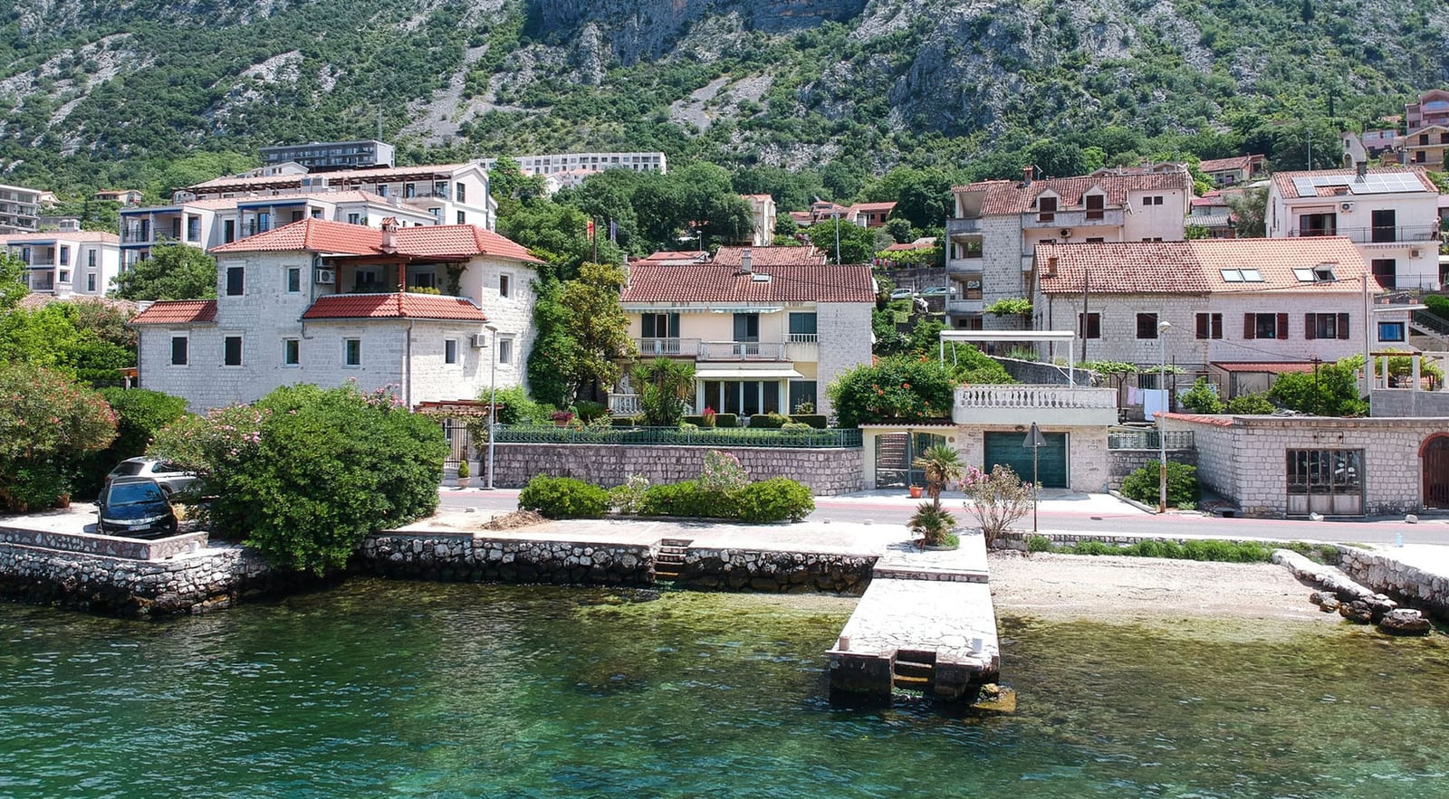Villa in Dobrota, Montenegro: Blick auf das Haus mit Steinverkleidung, privaten Steg und die Uferlinie der Bucht von Kotor.