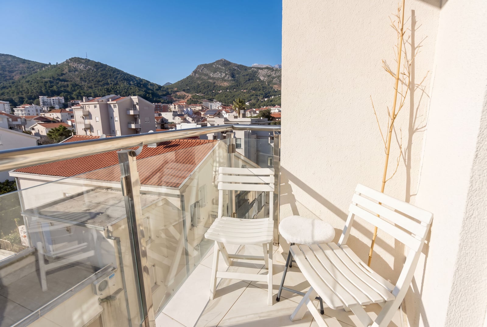 Balkon sa belim nameštajem i panoramskim pogledom na planine i grad u stanu u Budvi, Crna Gora