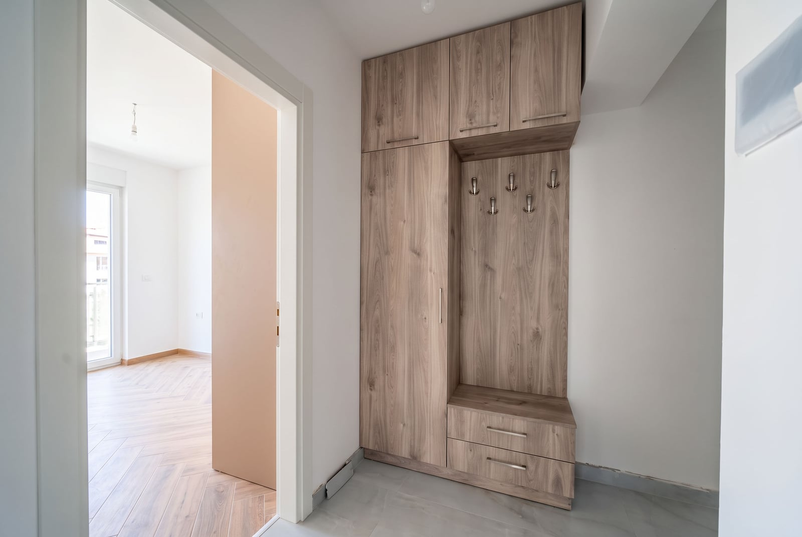 Entrance hall in a new apartment in Tivat, Montenegro: built-in wood-style wardrobe, light finishes, and a view into the living room.