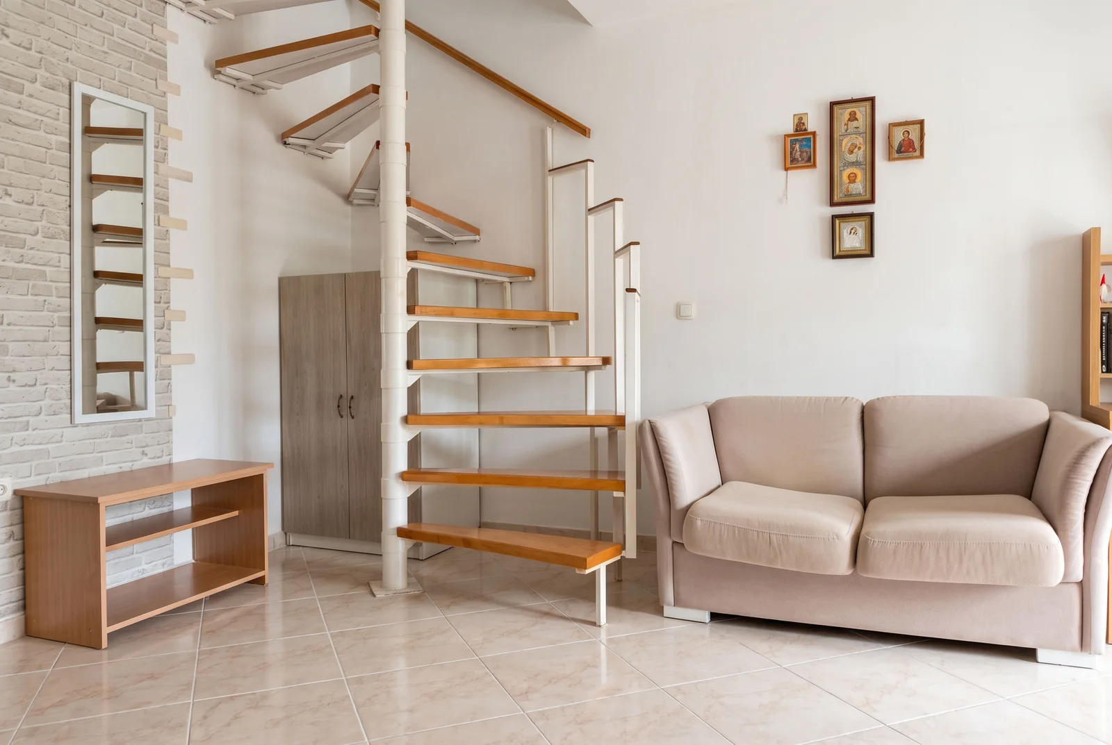 Living room featuring a beige sofa, spiral staircase with wooden steps, and religious icons on the wall.
