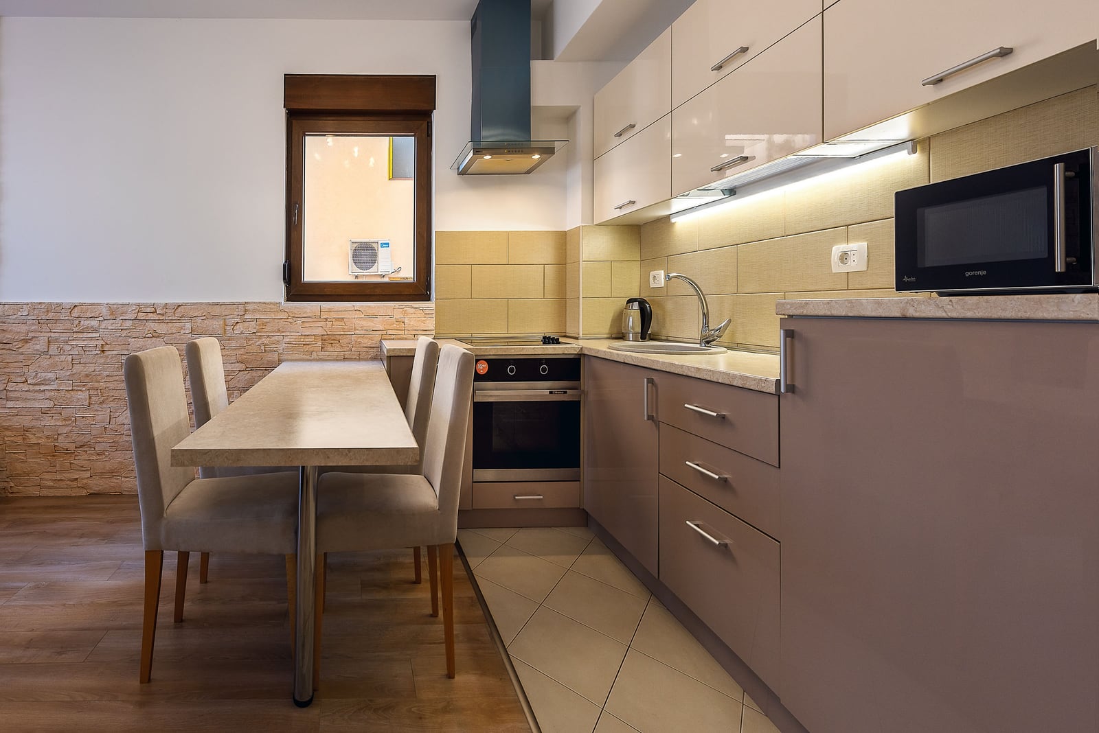 Modern kitchen in an apartment in Budva, Montenegro: glossy cabinetry, dining area, and natural stone finishes.