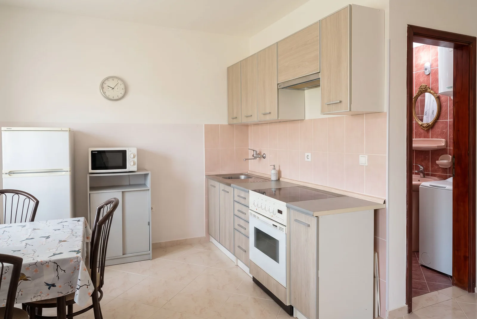 Kitchen with light wood cabinets, stove, fridge, and dining table; bathroom door visible on the right.