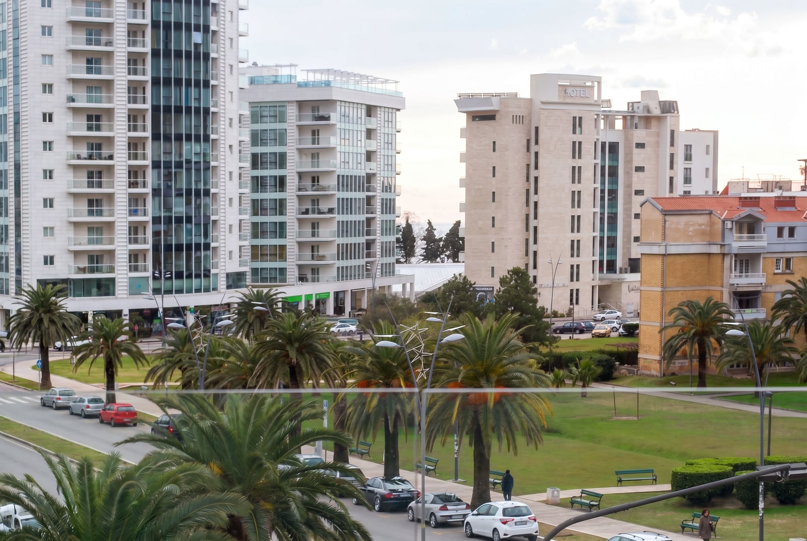 View from the window of modern residential complexes, a hotel, and a palm tree alley in the city of Budva, Montenegro.