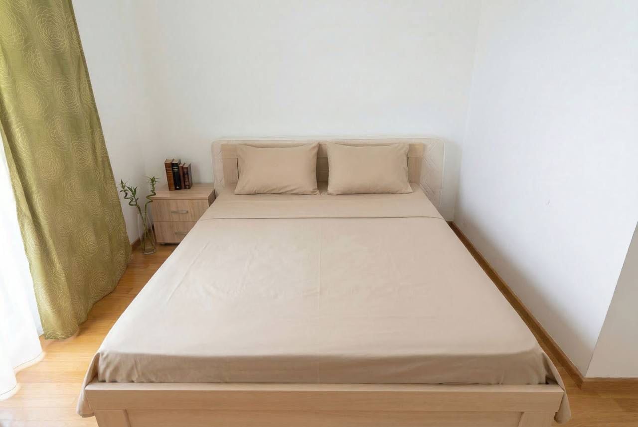Svetla spavaća soba sa bračnim krevetom u stanu u Bečićima, Crna Gora: minimalistički enterijer, parket i maslinaste zavese.