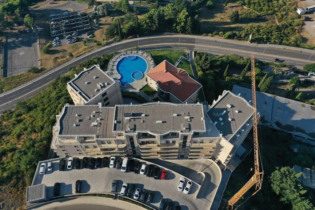 Aerial view of a residential complex in Bečići, Montenegro: swimming pool, parking, and modern building architecture.