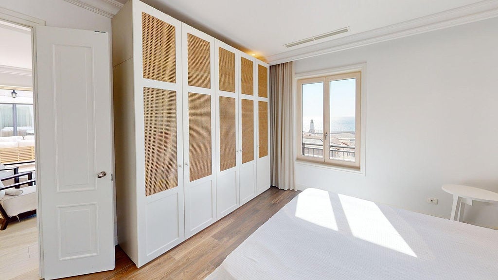 Spavaća soba u stanu, Luštica, Crna Gora: beli ormar sa rotang umetcima, svetli enterijer i pogled na more kroz prozor.