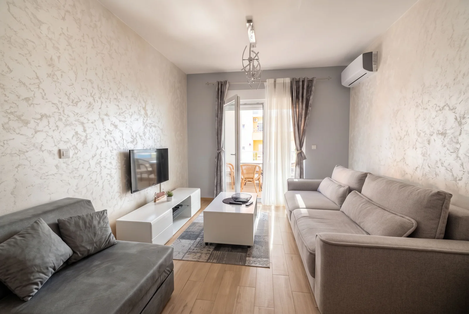Bright living room with grey sofas, white TV unit, and a door leading to a balcony.
