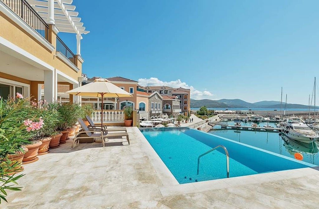 Bazen sa pogledom na marinu i jahte u stambenom kompleksu Luštica Bay, Crna Gora: terasa sa ležaljkama i suncobranom.