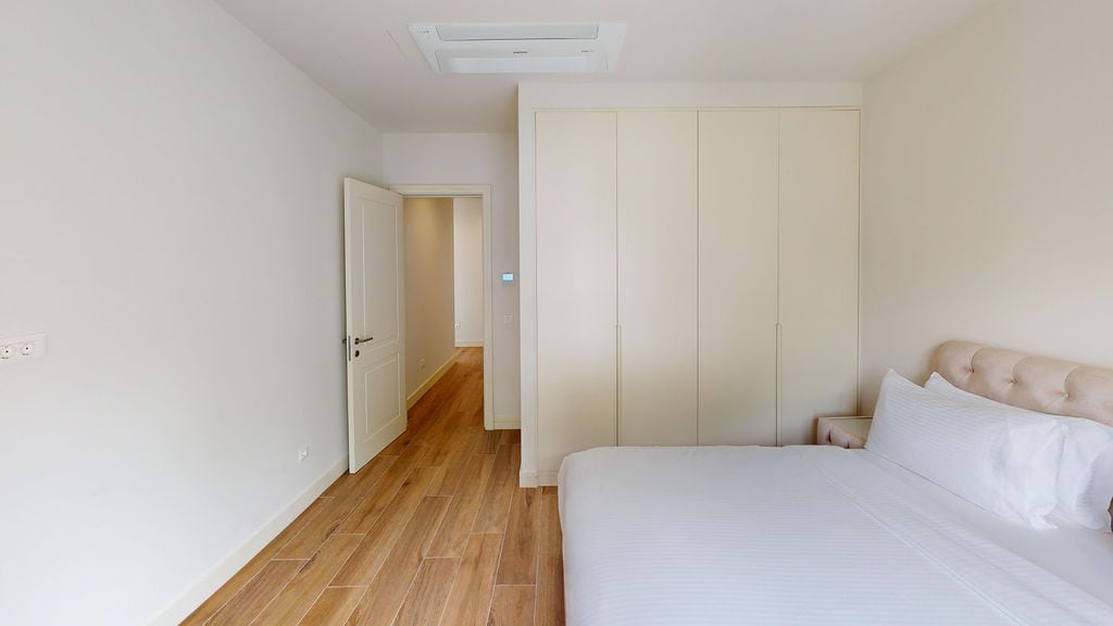 Светлая спальня в квартире Lustica Bay, Черногория: двуспальная кровать, встроенный шкаф и паркетный пол.
