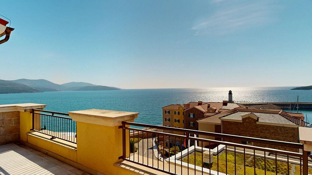 Pogled sa balkona na more i svetionik u stambenom kompleksu Luštica Bej, Crna Gora: terasa sa ogradom i panoramski pejzaž.
