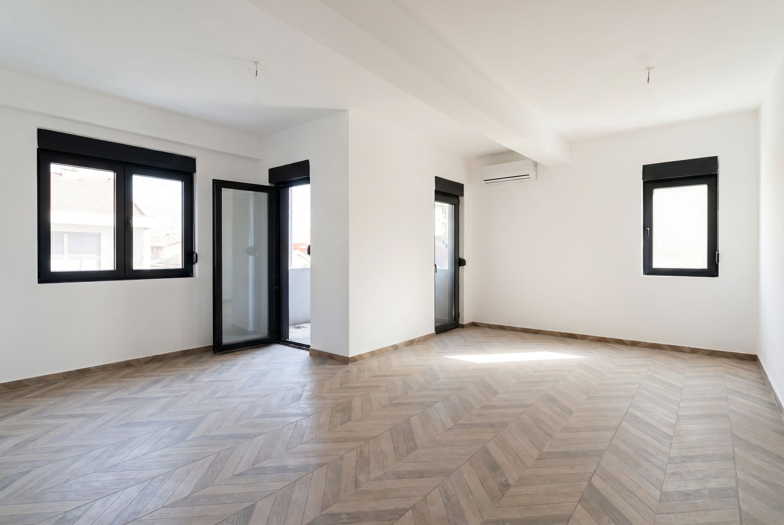 Svetla dnevna soba u novom stanu u Budvi, Crna Gora: beli zidovi, pod sa završnom obradom od drveta, panoramski prozori.