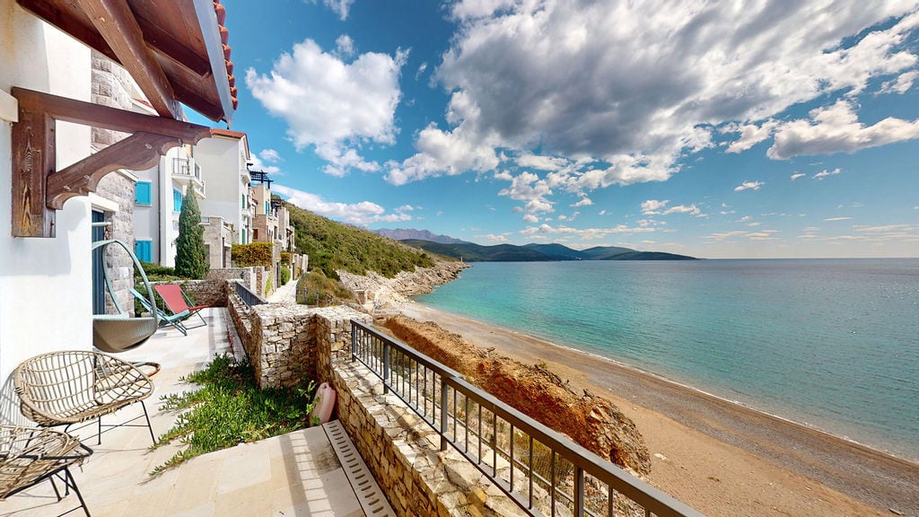 Karadağ, Luštica yerleşkesinde hasır mobilyalı teras ve deniz ile plajın panoramik manzarası.