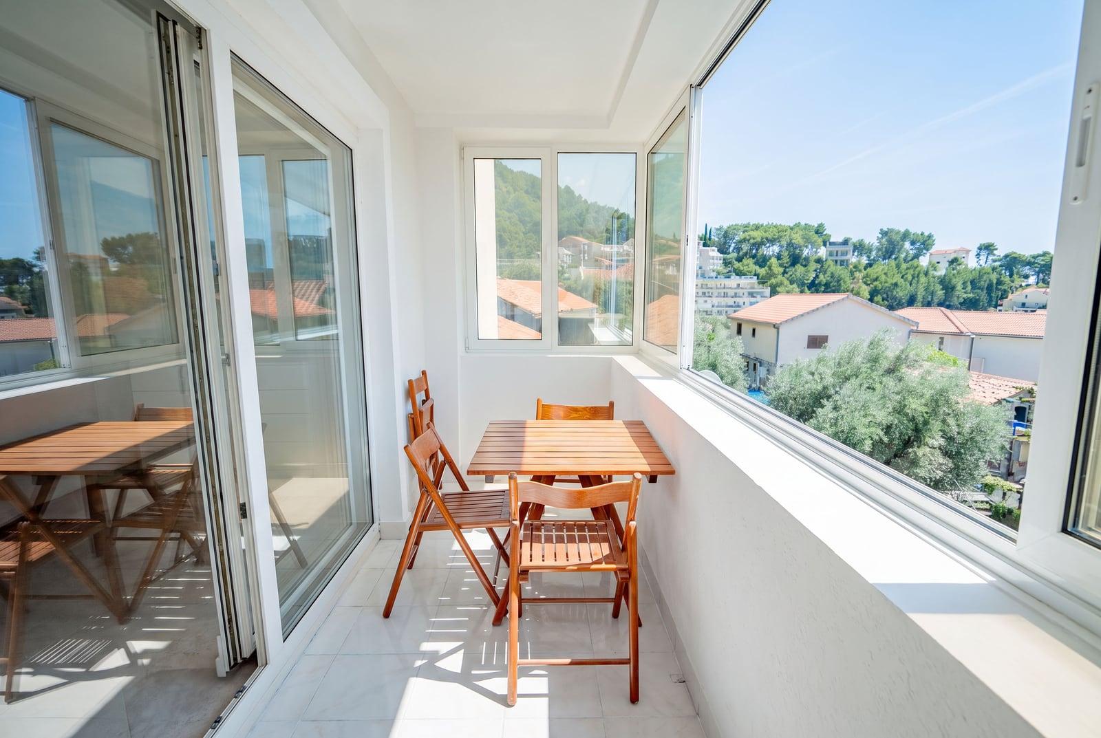 Bright balcony with wooden furniture and panoramic views of the mountains and the town of Sveti Stefan, Montenegro.