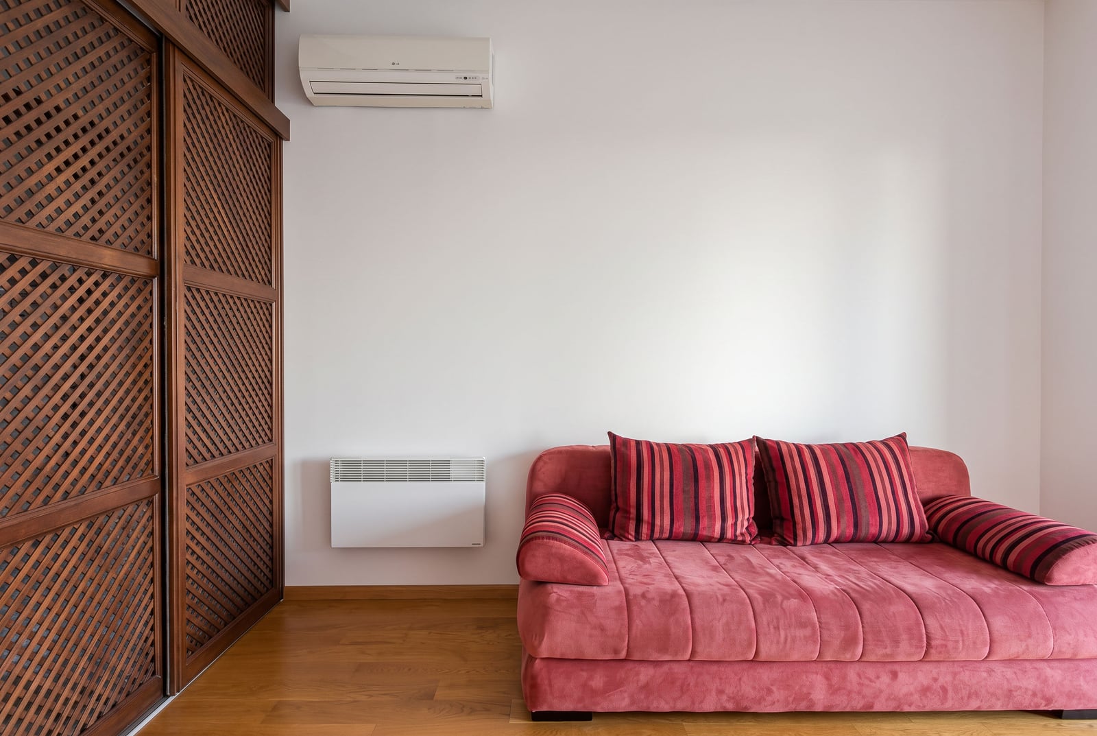 Living room with a red sofa, wooden wardrobe, and air conditioner in an apartment in Bečići, Montenegro.
