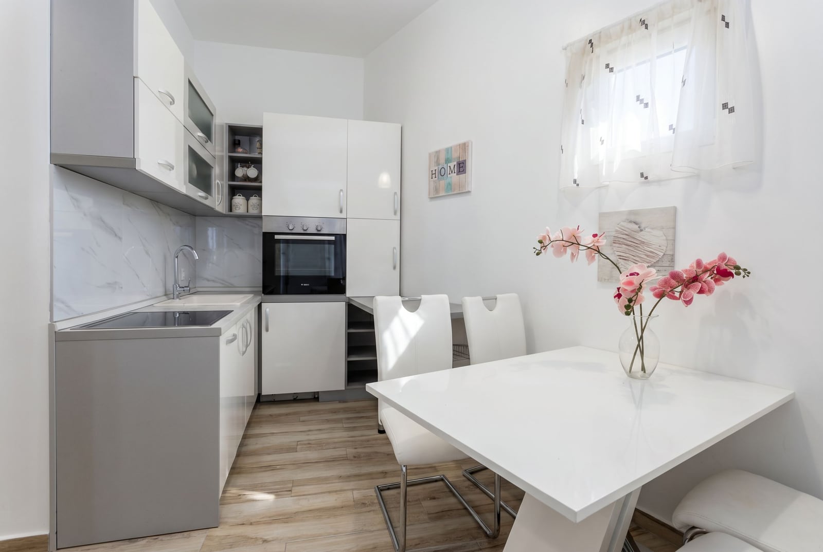 Moderne helle Küche in einer Wohnung in Bečići, Montenegro: weiße Einbauküche, Essbereich und hochwertige Ausstattung.
