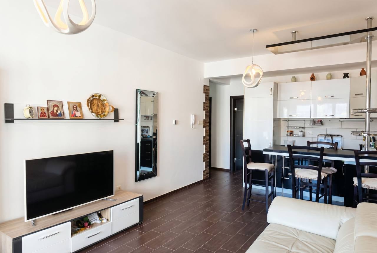 Modern living room with kitchen in an apartment in Budva, Montenegro: white furniture, TV area, and a bar counter.