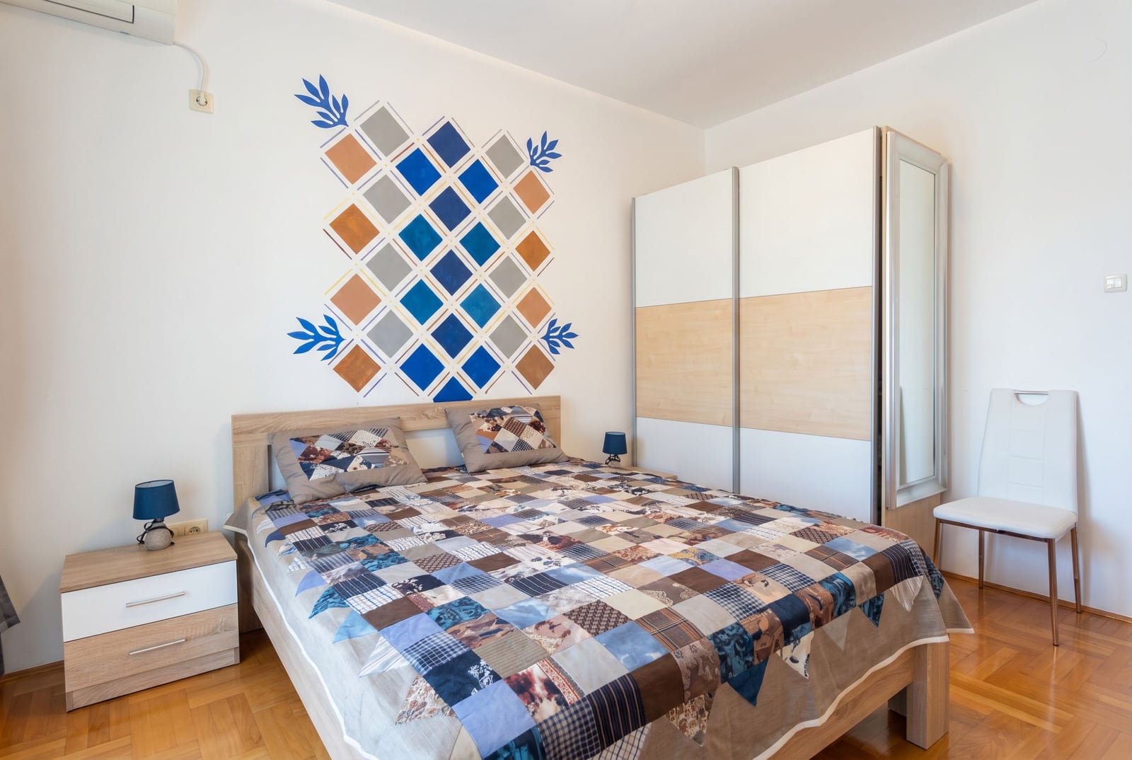 Bečići, Budva, Karadağ’daki dairede yatak odası: çift kişilik yatak, sürgülü gardırop ve patchwork tarzı duvar dekoru.