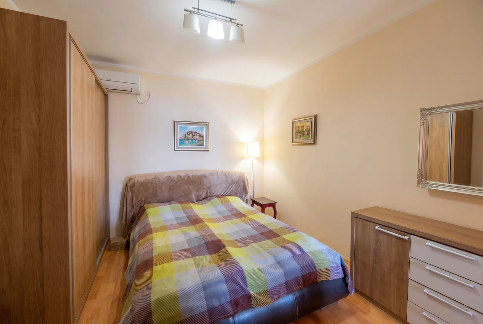 Chambre à coucher avec lit double, couverture à carreaux, armoire en bois et coiffeur avec miroir.