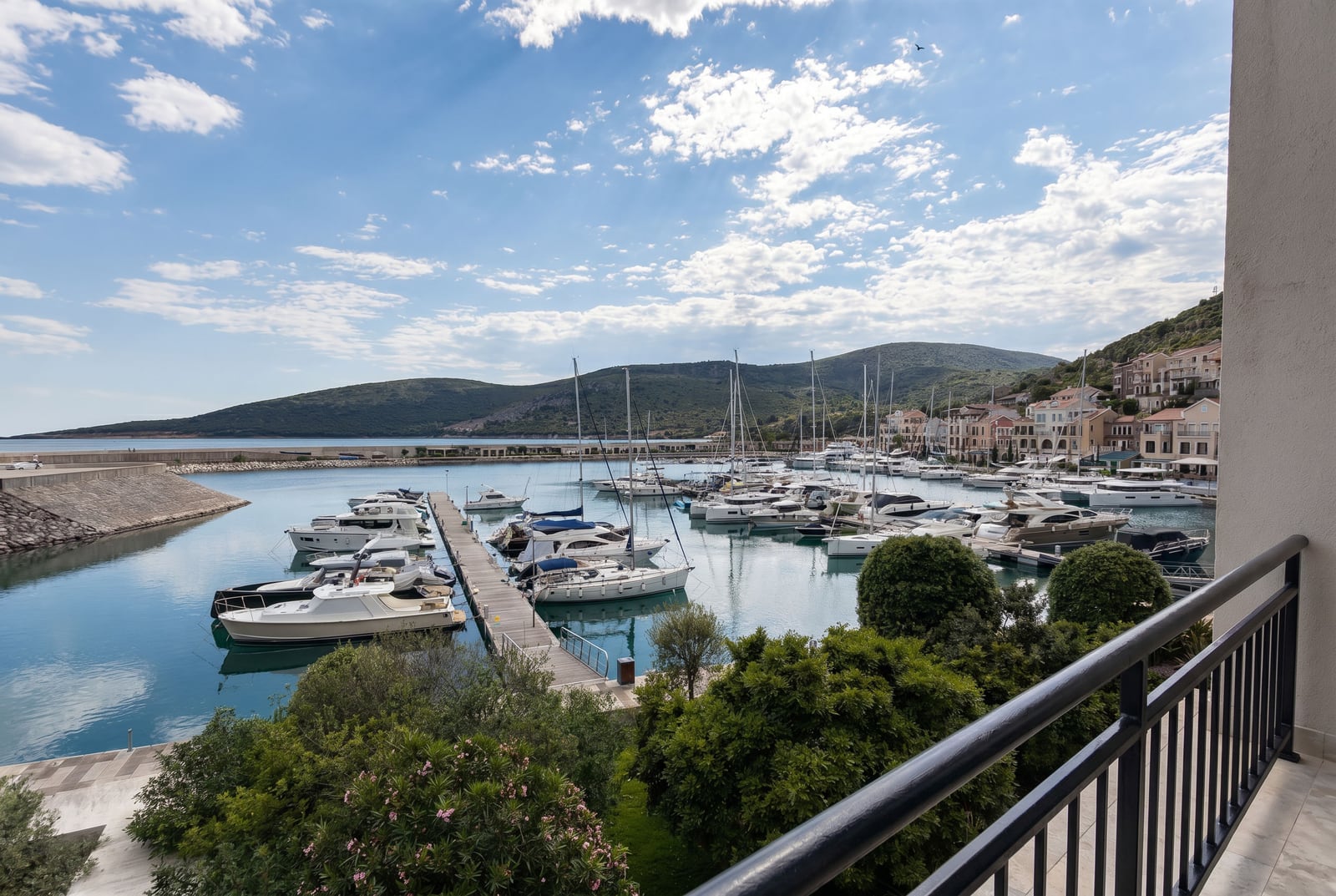 Blick vom Balkon auf den Yachthafen in Luštica Bay, Montenegro: Panorama der Bucht, Anlegestelle und Berge im Hintergrund.