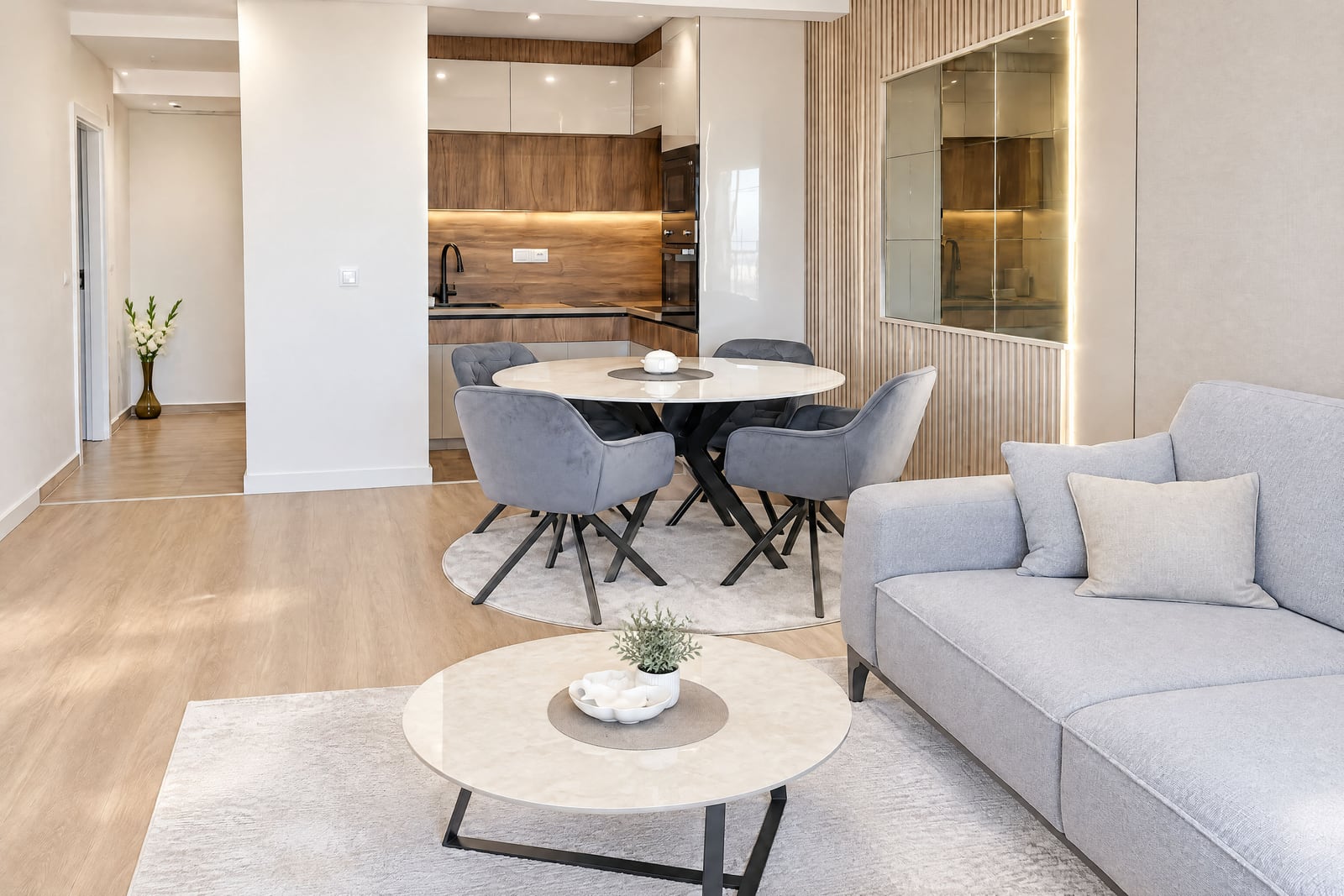 Modern living room with kitchen in an apartment in Budva, Montenegro: gray-beige interior, soft sofa, round dining area ...