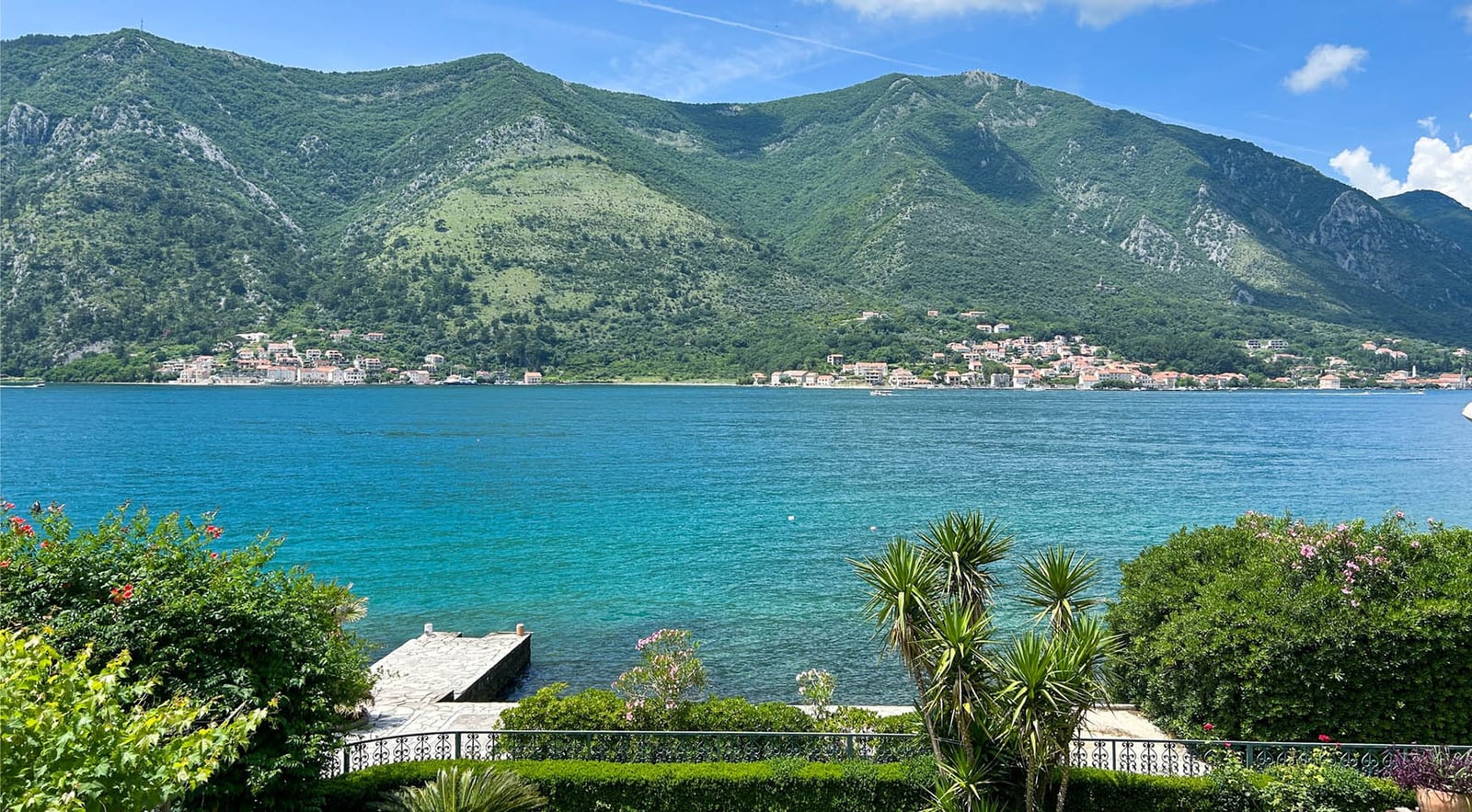 Panoramablick auf die Bucht von Kotor und die Berge von der Terrasse der Villa in Dobrota, Montenegro: privater Steg und blühender Garten.