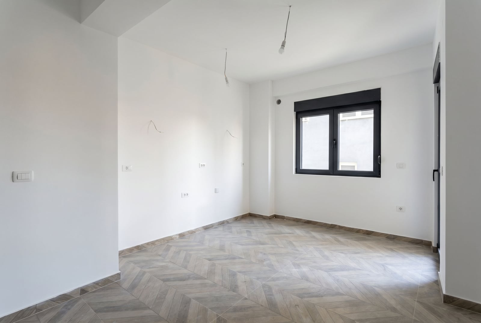 Svetla dnevna soba u novom stanu u Budvi, Crna Gora: beli zidovi, pod sa završnom obradom u imitaciji drveta, crni prozor.