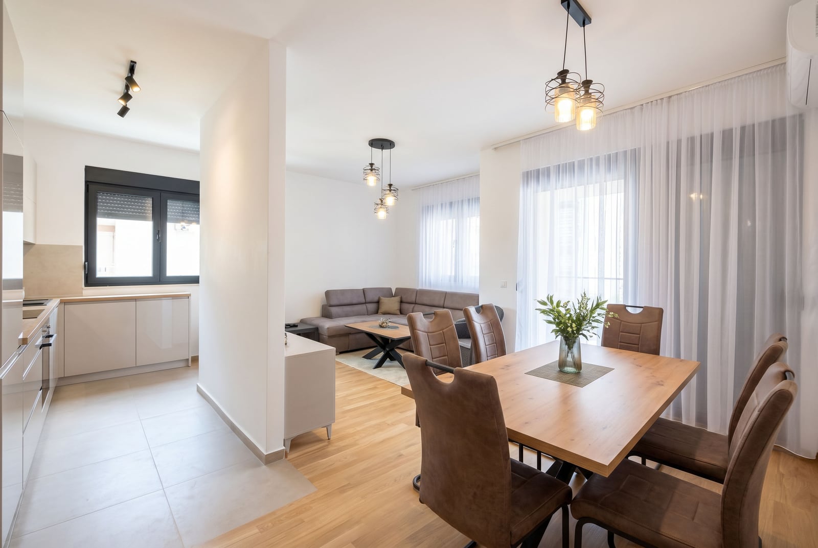 Modern living room with a kitchen in a Budva apartment, Montenegro: dining area, sectional sofa, and bright interior.