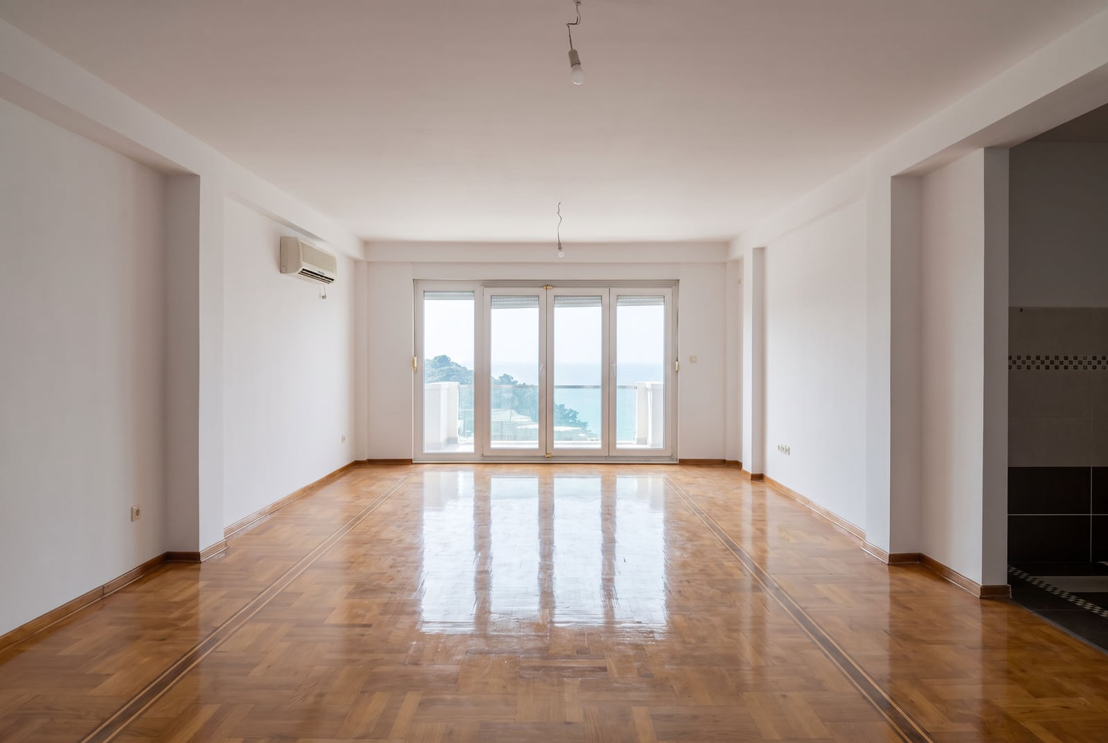 Bright empty living room with parquet flooring, air conditioning, and a panoramic window with sea view in an apartment in Petrovac, Montenegro.