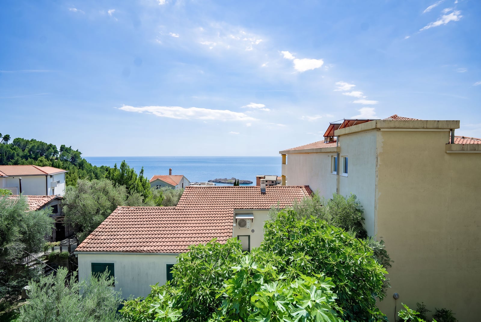 Panoramic view of the sea and tiled rooftops in Sveti Stefan, Montenegro, surrounded by greenery and Mediterranean trees.