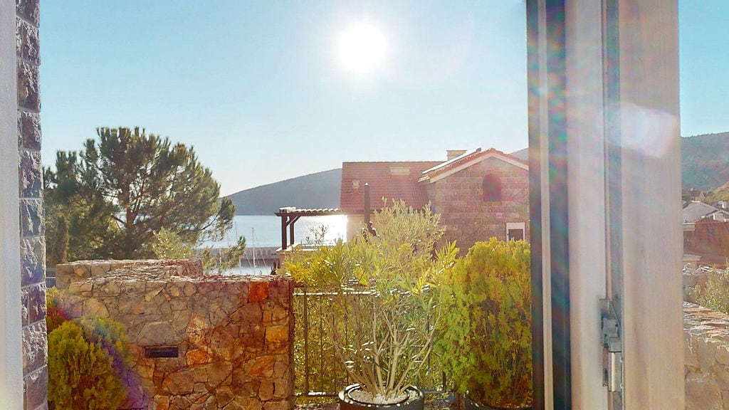 Blick von der Terrasse auf das Meer und die Yachthafenanlage in der Wohnanlage Luštica, Montenegro: Steinverkleidung und mediterrane Pflanzen.