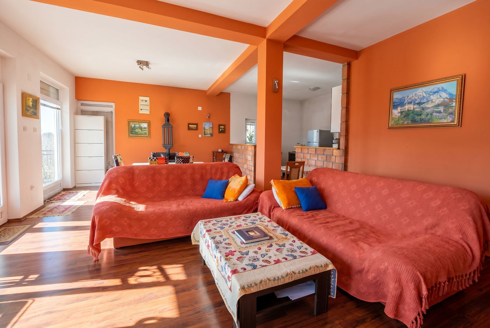 Living room with orange walls and upholstered furniture in a house, Buljarica, Montenegro. View of the lounge area and kitchen.