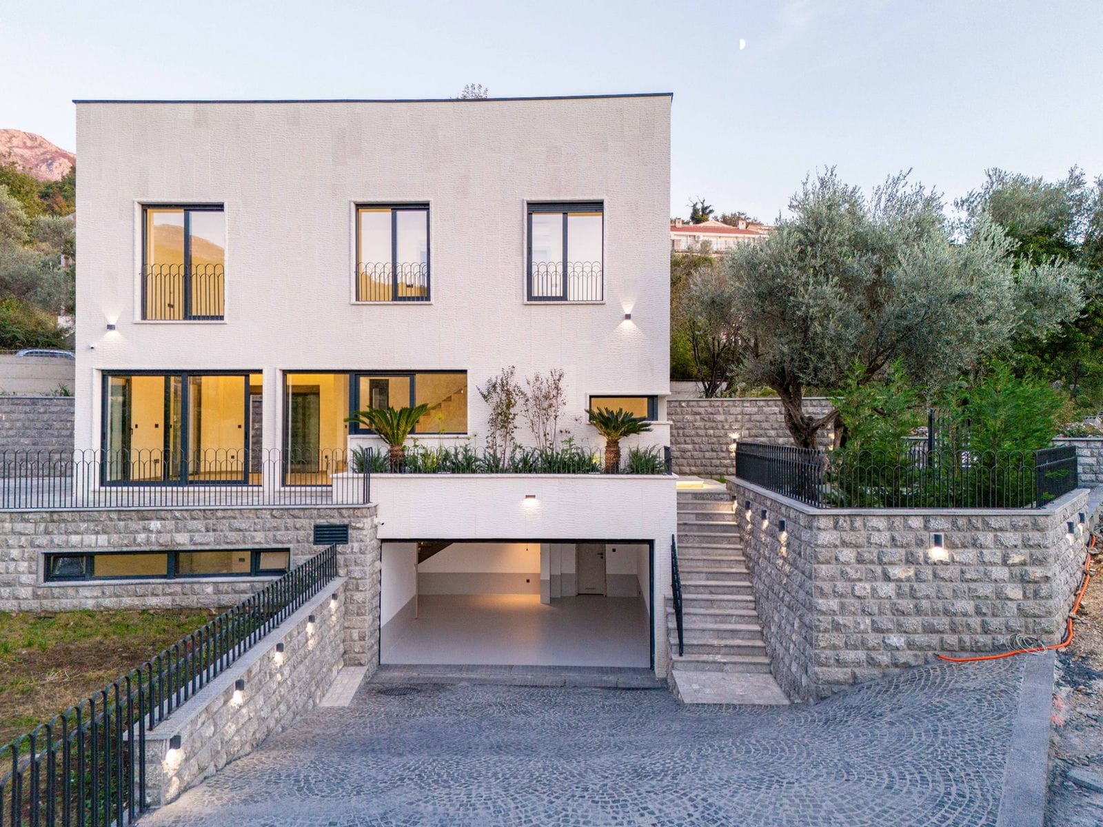 Villa moderne à Kamenovo, Monténégro : façade avec fenêtres panoramiques, terrasse, aménagement paysager et garage.