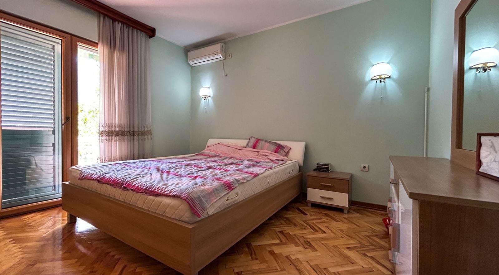Schlafzimmer mit Doppelbett und Parkett in einer Villa in Dobrota, Montenegro: Blick auf die Terrasse und Holzmöbel.