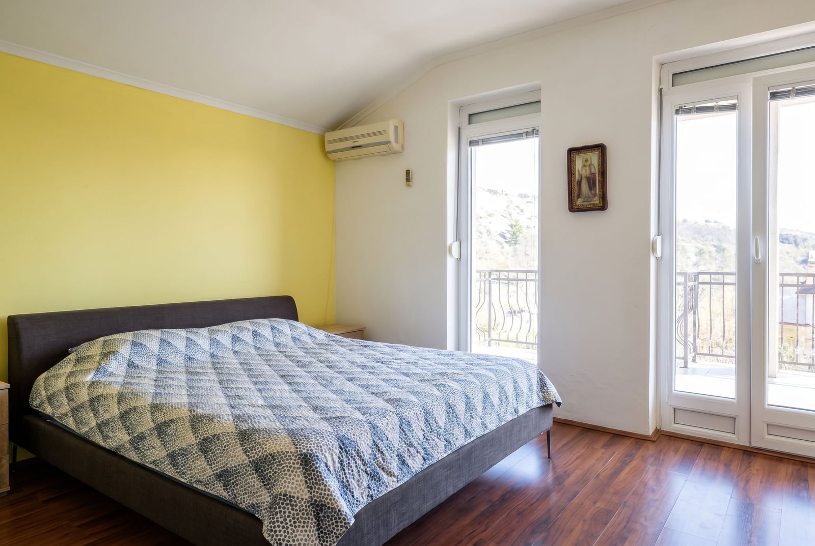 Bedroom with a double bed, yellow accent wall, and balcony access in a house in Buljarica, Montenegro.
