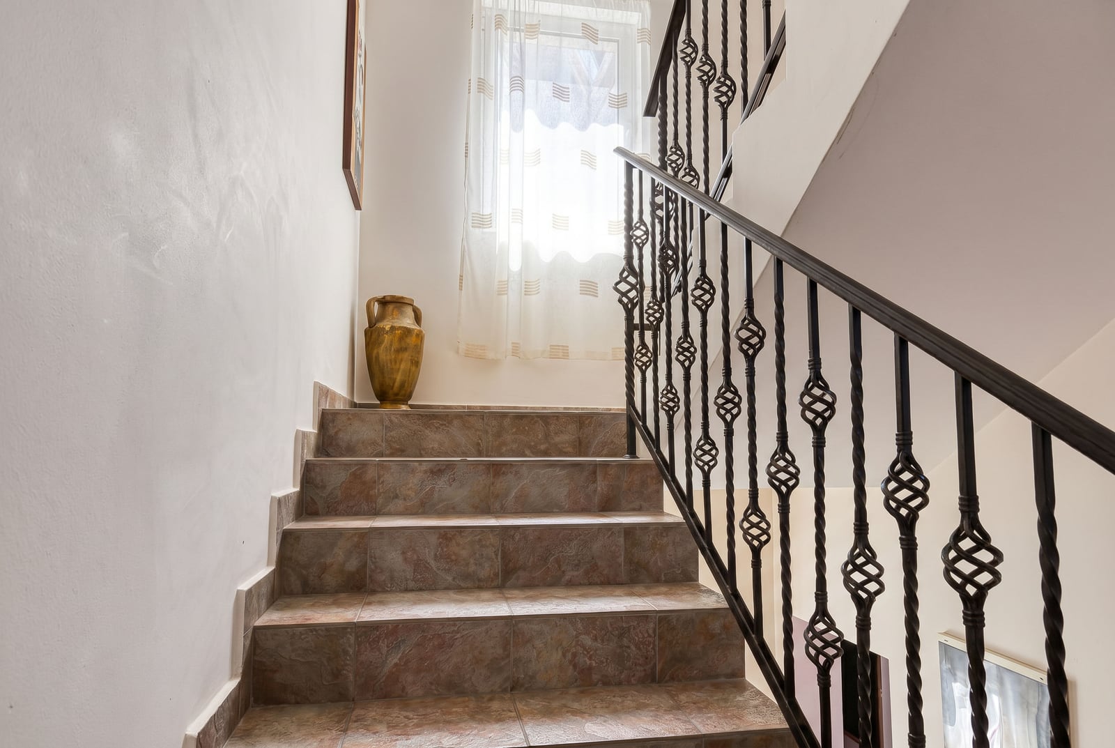 Escalier avec rampe en fer forgé et carrelage en céramique dans une villa à Bečići, au Monténégro. Intérieur de la maison avec vase décoratif.