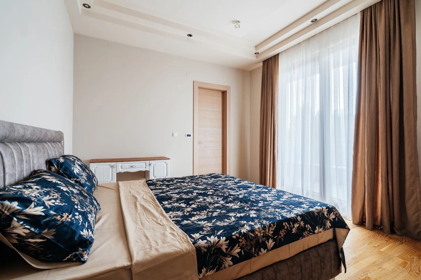 Svetla spavaća soba sa bračnim krevetom i panoramskim prozorom u modernom stanu, grad Budva, Crna Gora.